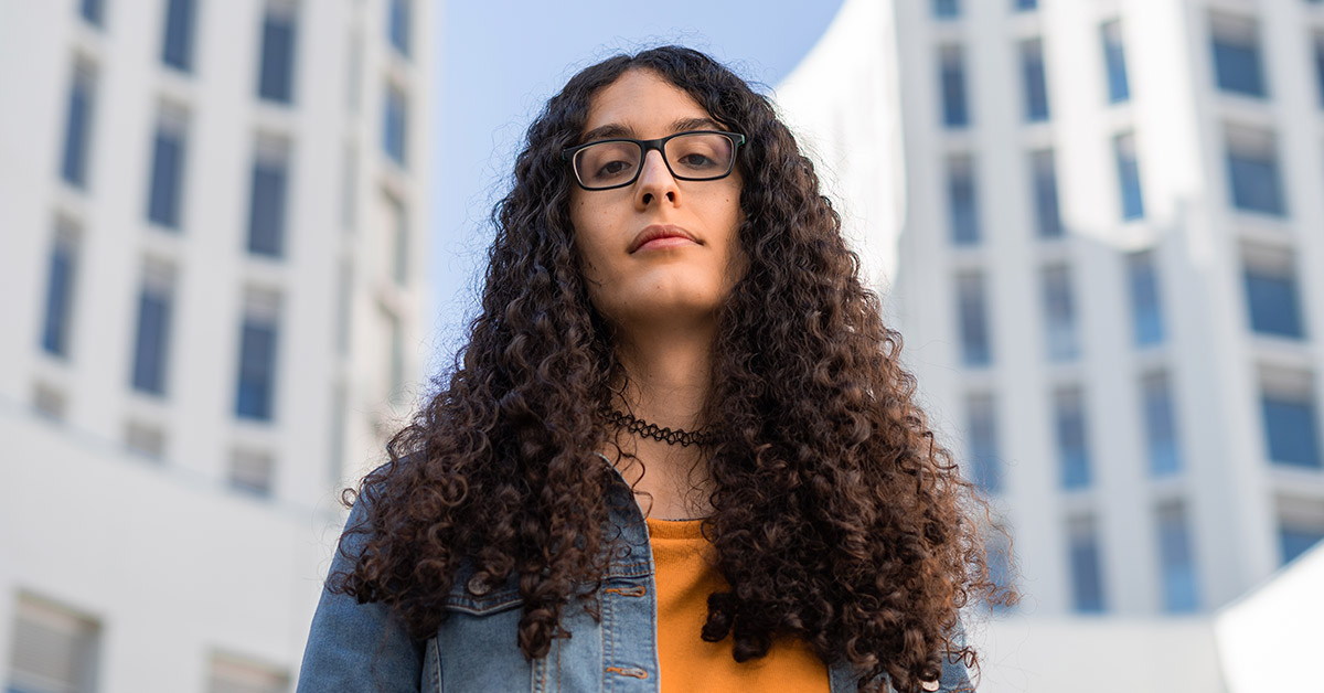 young person with glasses, dark long curly hair longer downwards