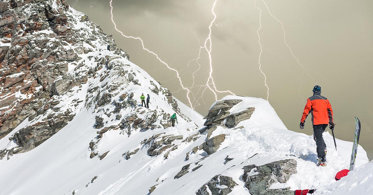 person walking on snowy mountain peak with lighting piercing through the sky