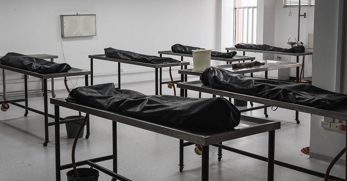 various dead bodies in black bags on metal tables