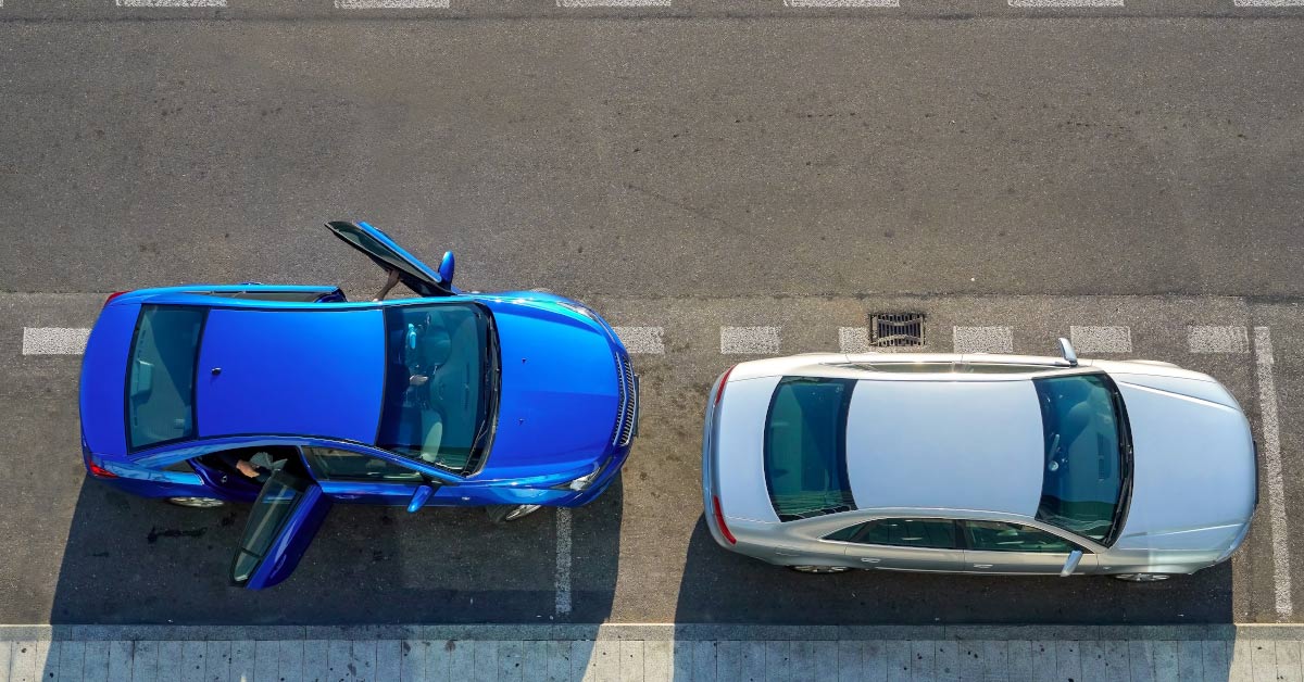 two parked cars seen from above. One blue one grey. The blue car has one of its doors open facing the road. Open car doors facing the road can increase the chances of cyclist injury known as dooring